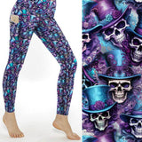 A pair of full-length leggings featuring a vibrant pattern with skulls wearing purple and turquoise top hats against a silver background.