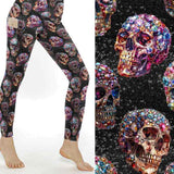 Leggings featuring vibrant gemstone skulls in pink, blue, and gold hues against a glittering black background.
