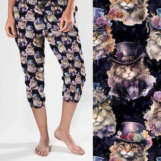 A pair of capri joggers featuring a colorful print of various cats wearing Victorian-style clothing, including top hats and bow ties, on a dark background.