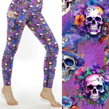 Mockup of 'Til Death Do We Party Skull Leggings with colorful skulls, flowers, and wizard hats on a purple background; close-up shows vivid details by Nikki Whoops Boutique.