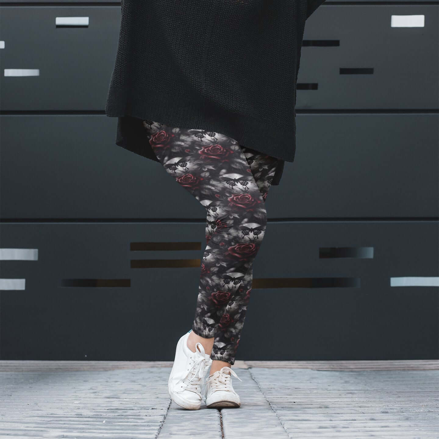 Person wearing floral leggings with a black coat and white sneakers against a dark background
