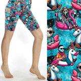 A pair of sport shorts with a vibrant print featuring characters from horror movies, such as Ghostface and Chucky, in a tropical setting with pool and unicorn floaties.