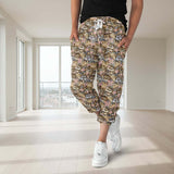 Person in an empty living room wearing capri jogger pants featuring cartoon glam cats wearing glasses and leopard accessories, holding takeaway coffees. Surrounded by animal print bows, handbags, and a sparkly grey and pastel pink background.