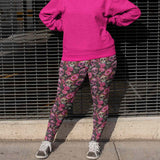Person wearing a bright pink hoodie and patterned pants standing against a metal fence.