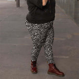 Person wearing leopard print pants and red boots on a grey pavement.