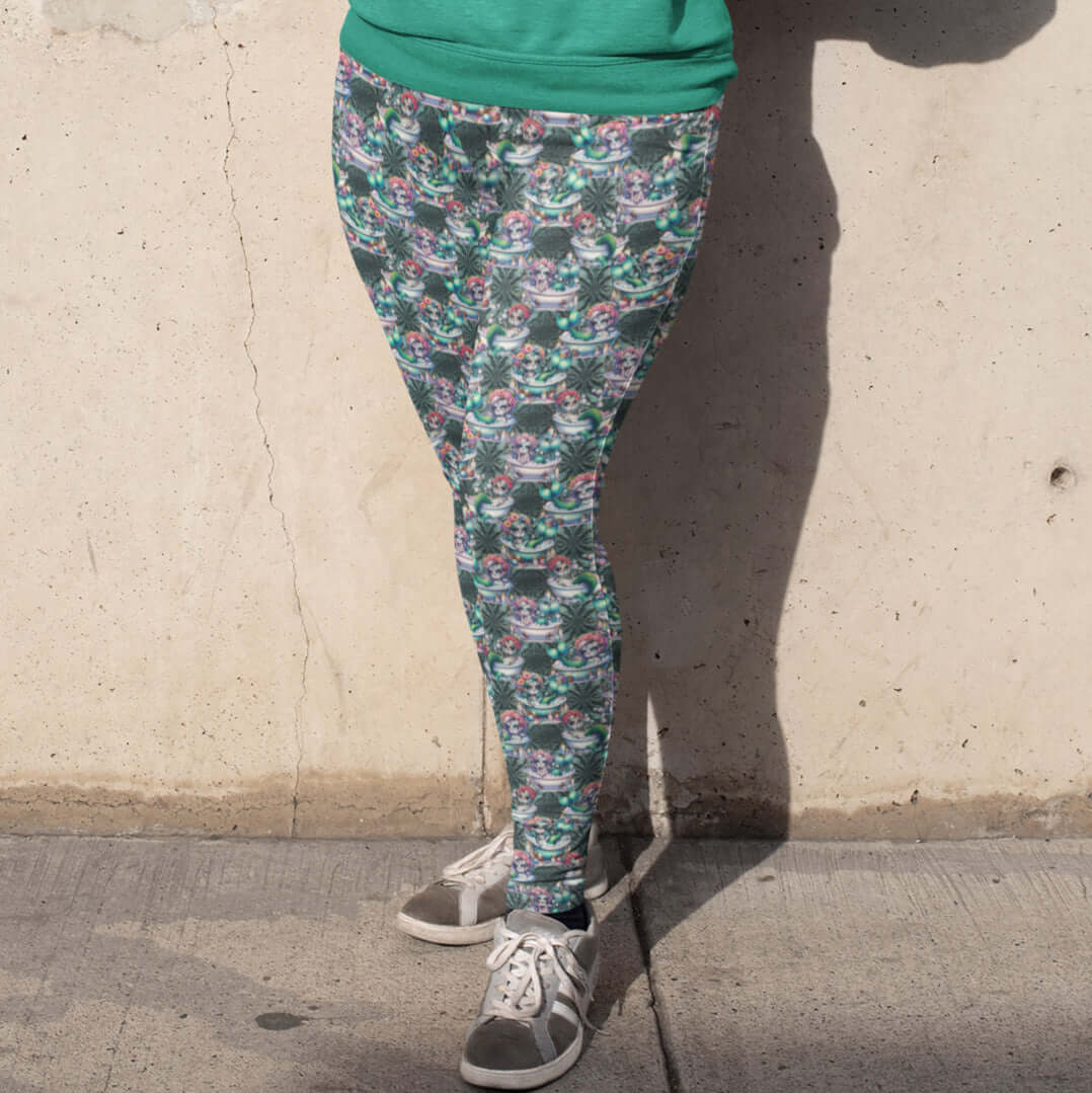 girl standing against a wall wearing leggings featuring a whimsical design with mermaids, sea creatures, and Day of the Dead-inspired makeup and garlands.