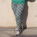 girl standing against a wall wearing leggings featuring a whimsical design with mermaids, sea creatures, and Day of the Dead-inspired makeup and garlands.