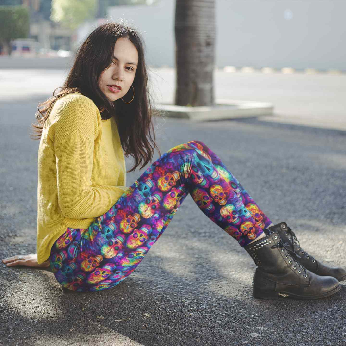 Person wearing a yellow sweater and colorful rainbow skull-patterned leggings sitting on the ground.