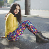 Person wearing a yellow sweater and colorful rainbow skull-patterned leggings sitting on the ground.