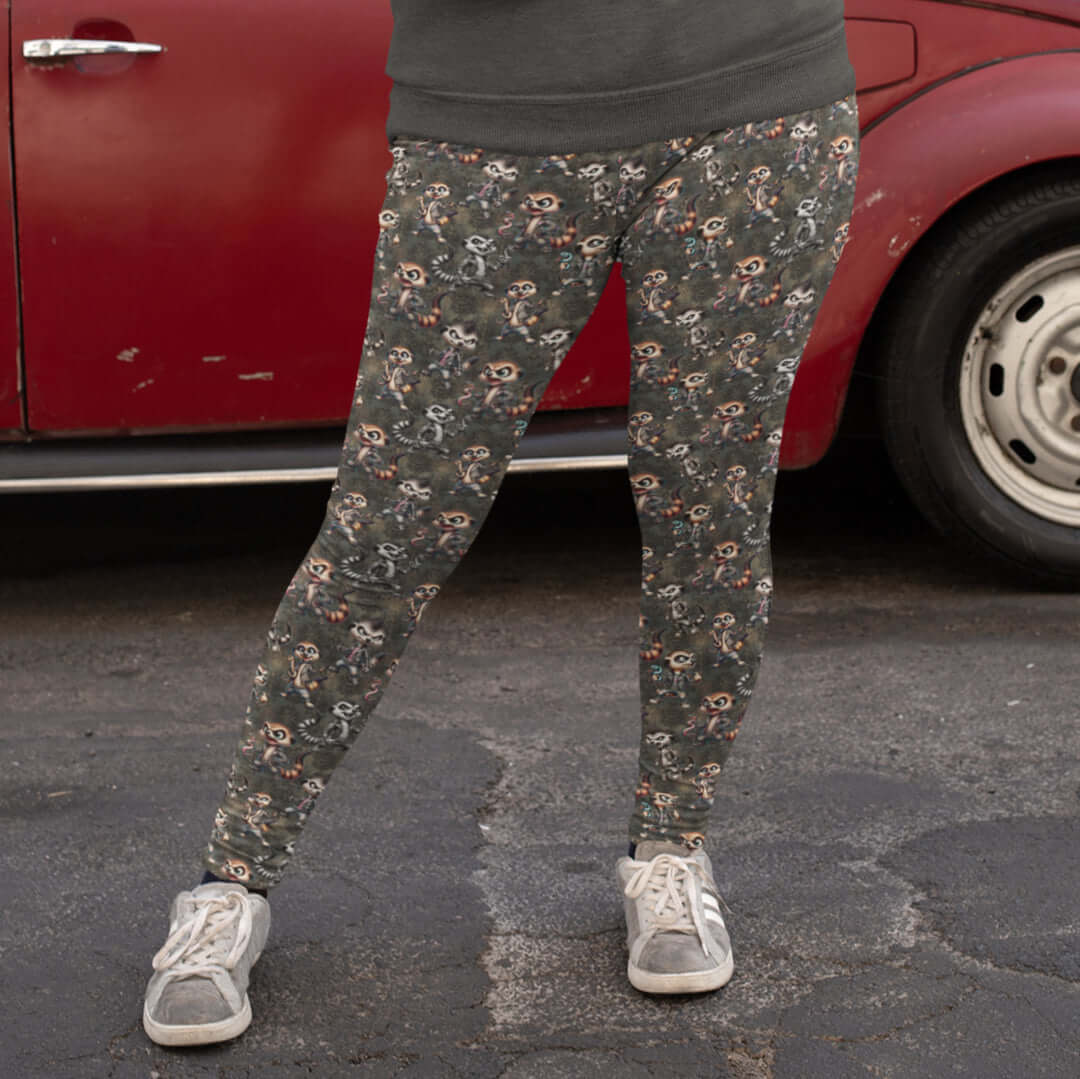 girl standing in front of a red car wearing leggings featuring a pattern with cartoon-style meerkats in punk fashion, including skulls and mohawks, displayed alongside a side pocket with a phone.