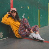 Woman sitting against a green wall wearing a yellow sweatshirt, raccoon leggings, and white sneakers.
