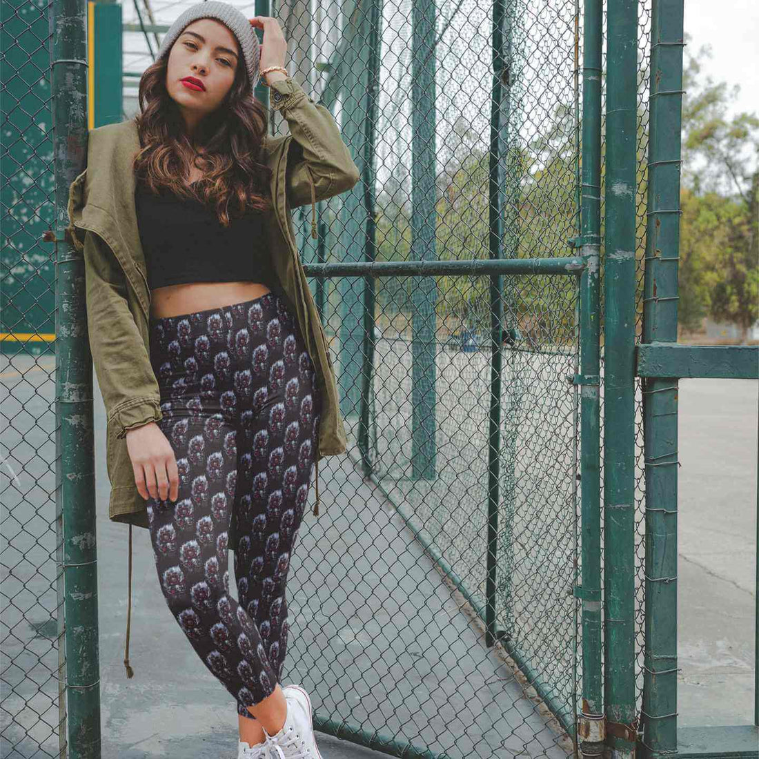 Woman wearing Death Petal skull print leggings at a basketball court fence, Nikki Whoops Boutique