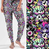 Full length jogger pants featuring colourful punk-inspired teddy bears, rainbow skulls, bats, spiderwebs and neon alternative artwork on a black background with bright pink, purple, green and blue accents.