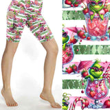 Christmas sports shorts featuring a green Grinch-like character lounging in pink cocktail glasses on a pink and white striped background with fruit and candy canes by Nikki Whoops Boutique.