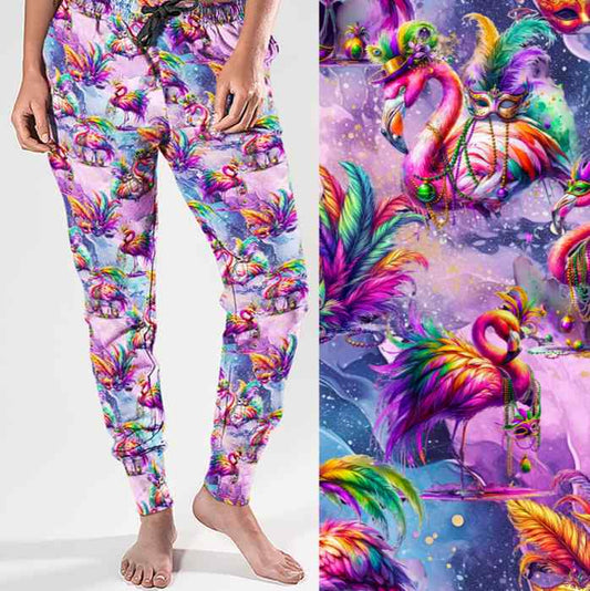 mockup of Full-length jogger pants featuring vibrant pink flamingos dressed in colourful Mardi Gras-style feathers and accessories. The background is a swirling galaxy of purples, pinks and blues with stars and glittery textures.