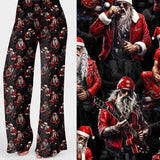 Wide leg Christmas lounge pants featuring a tattooed Santa in a red leather jacket playing guitar under stage lights on a black background by Nikki Whoops Boutique.