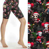 Black Christmas sports shorts with chibi horror icons Freddy, Jason, Michael, Pennywise and Chucky in Santa outfits surrounded by gold stars and lights by Nikki Whoops Boutique, next to a close-up of the pattern.