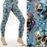 Light blue leggings with a pattern of skulls, butterflies, and pastel flowers. A close-up shows detailed skulls adorned with butterflies and floral arrangements. The leggings are high-waisted with a side pocket holding a phone, and have a full-length fit. The design is vibrant and whimsical, blending gothic and delicate elements