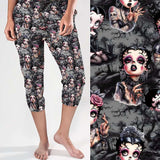 Capri jogger pants featuring a gothic cartoon print of heavily tattooed, pin-up inspired women with dramatic makeup. Background includes gravestones, thorny trees and a dark grey atmosphere.