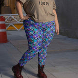 person in colorful christmas-themed Jack & Sally leggings, beige T-shirt, and burgundy boots on gray pavement.