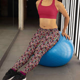 A person wearing patterned leggings with a comic-style design and a red sports bra, leaning back on a blue exercise ball in a gym setting. Black sneakers and purple socks complete the outfit. The background includes a mirrored wall and striped lighting, creating a modern workout atmosphere.