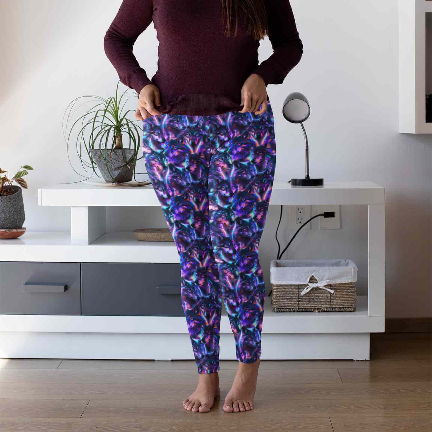 Person wearing colorful of Dances With Wolves leggings with neon purple, blue, and pink wolf print, high waistband, and side pocket wolf patterned leggings in a room with a white cabinet and plants by Nikki Whoops Boutique.