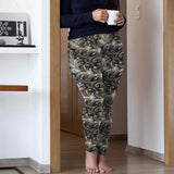 Person wearing gold and black leggings holding a cup in a home setting.