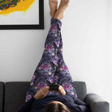 Person lying on a couch, legs up, wearing dark leggings with purple floral pattern; using a phone.