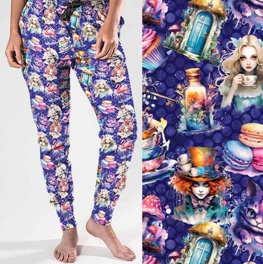 Full-length jogger pants mockup featuring an Alice in Wonderland theme. The design includes vibrant illustrations of Alice, the Mad Hatter, Cheshire Cat, teacups, mushrooms, potion bottles and macarons on a deep purple background.