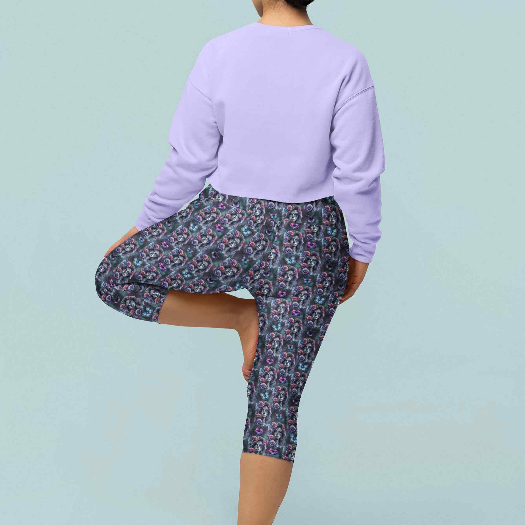 Gothic Glamour capri leggings on girl in tree pose. Elegant La Catrina images in grey blue tones. Pink and purple roses in her hair, surrounded by flowers and butterflies.