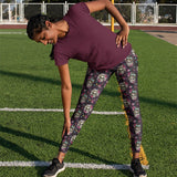 Person stretching on grass while wearing Audrey Hepburn Marilyn Monroe skull-patterned leggings and a purple top