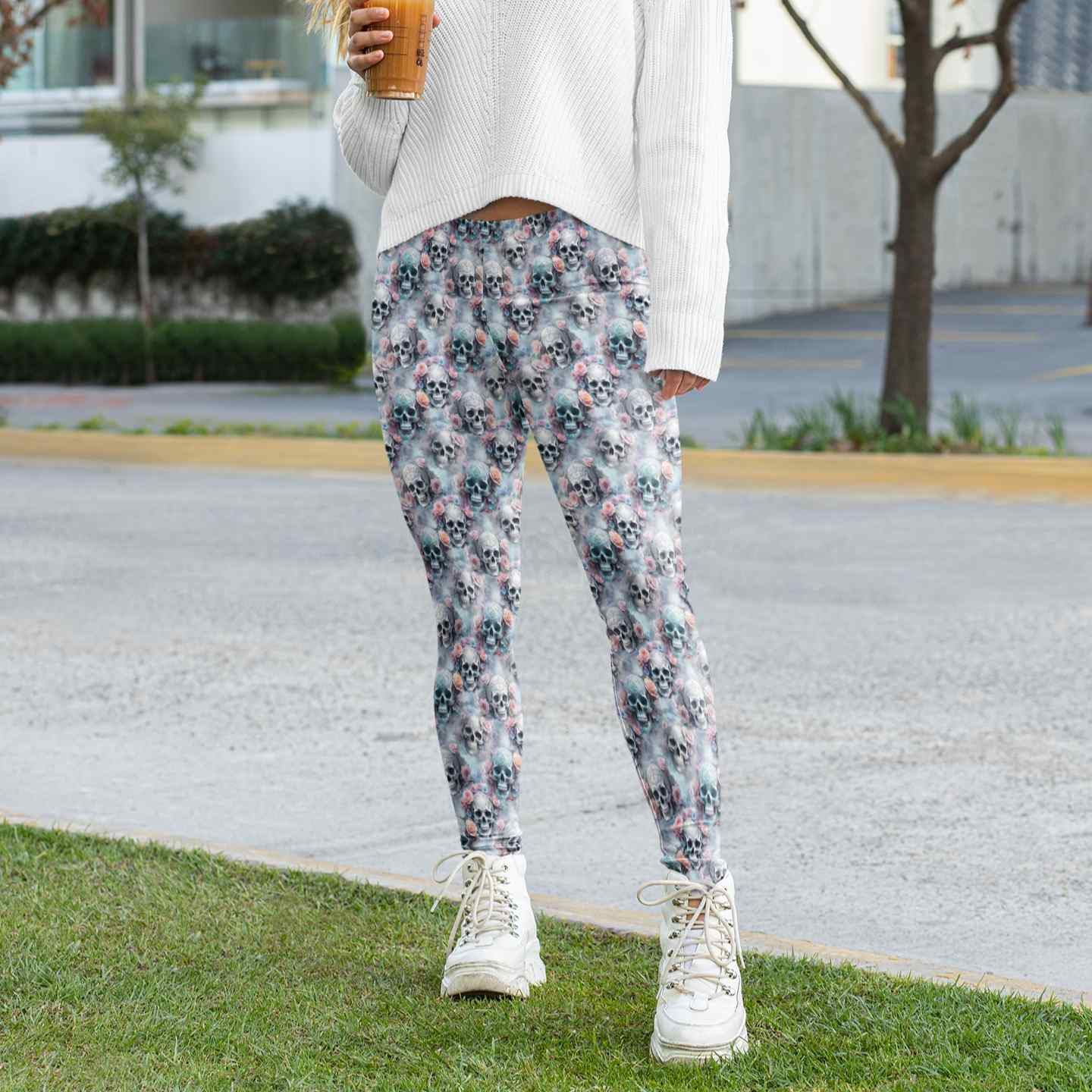 Person wearing floral pants and white sneakers standing on grass with a blurred background