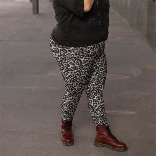 Person wearing leopard print pants and red boots on a grey pavement.