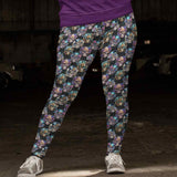 Steampunk souls capri leggings on a woman standing in a garage. steampunk skulls wearing flowers and top hats. Shades of pink, purple and turquoise on a distressed black background