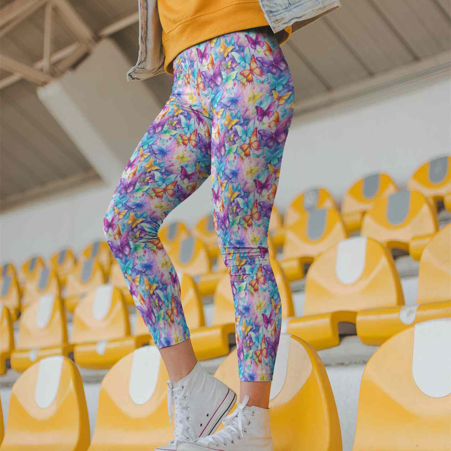 Person wearing colorful butterfly-patterned leggings standing in an indoor setting with yellow chairs.